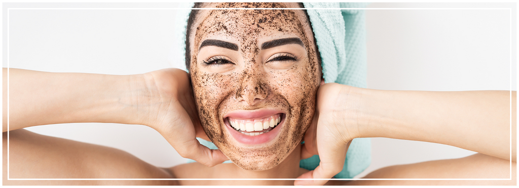 ragazza con accappatoio in testa che sorride con una maschera esfoliante sul viso